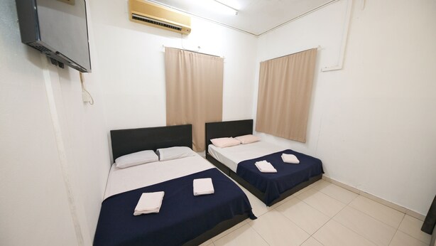 A room with two beds, each with a dark blue bedspread and white pillows. There is a flat-screen TV mounted on the wall, an air conditioning unit above the beds, and a window with beige curtains. - Hotel O Innap Kota Bharu (Kota Bharu)