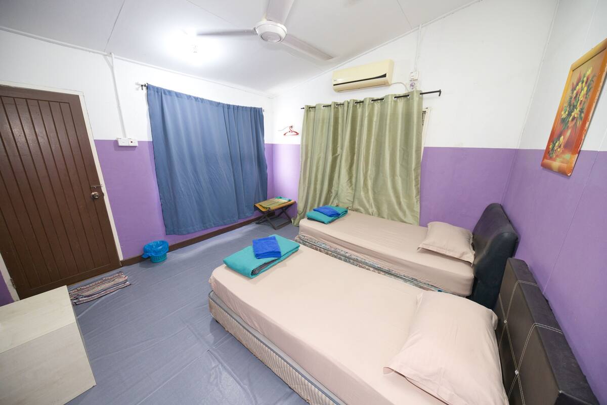 A room with two beds, a ceiling fan, an air conditioner, and a door.