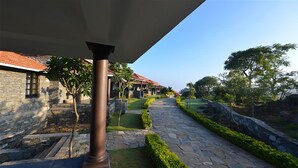 A stone pathway leading to a building with a red-tiled roof, surrounded by greenery and stone walls. - The Wild Retreat (Kumbhalgarh)