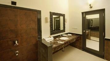 Un baño moderno con tocador de mármol oscuro, un espejo grande y un lavabo independiente.
