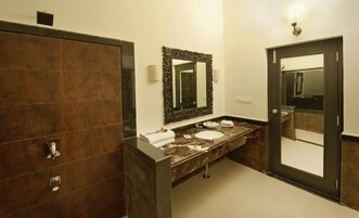 Un baño moderno con tocador de mármol oscuro, un espejo grande y un lavabo independiente.