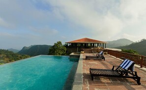 A pool area with a clear view of the mountains, a covered seating area, and a lounge chair. - The Wild Retreat (Kumbhalgarh)