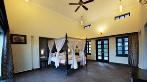 A spacious bedroom with a four-poster bed, a ceiling fan, and multiple windows. - The Wild Retreat (Kumbhalgarh)