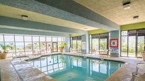 Une piscine intérieure avec des parois en verre transparent, un panneau indiquant la présence d’un sauveteur et une vue sur l’extérieur.