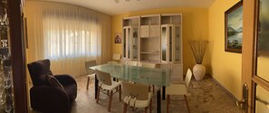 Un comedor con una mesa de vidrio, sillas, un armario con puertas de cristal y un jarrón con cañas.