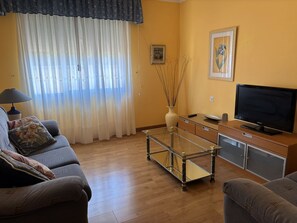 Una sala de estar con un sofá, una mesa de centro de vidrio, un televisor y un aparador.