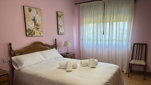 Una cama bien hecha con sábanas blancas, un cabecero de madera, una mesita de noche con una lámpara y una silla.
