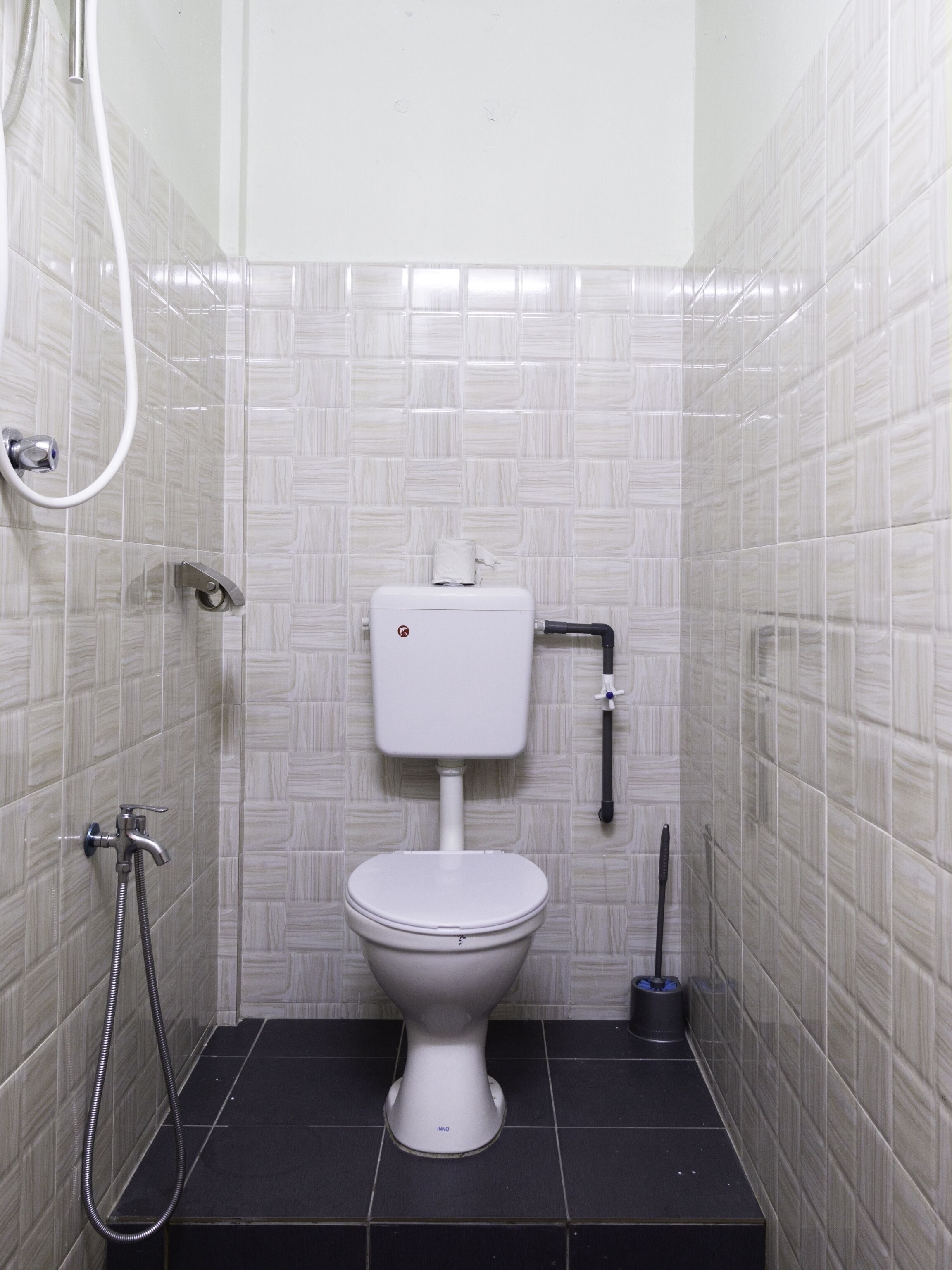 A small, tiled bathroom with a white toilet, a showerhead, and a bidet.