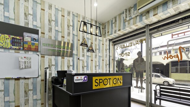 A reception desk with a 'SPOT ON' sign, a whiteboard with notes, and a wooden floor. - Hotel O City Hostel Ipoh (Ipoh)