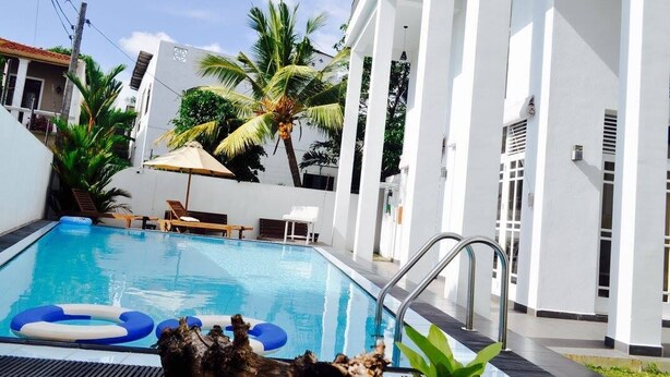 Ein Swimmingpool mit Liegestühlen und einer Palme, umgeben von weißen Gebäuden.