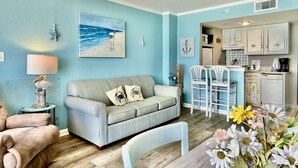 Ein Wohnzimmer mit hellblauer Wand, einem grauen Sofa mit dekorativen Kissen, einem weißen Couchtisch und einer Blumenkomposition.