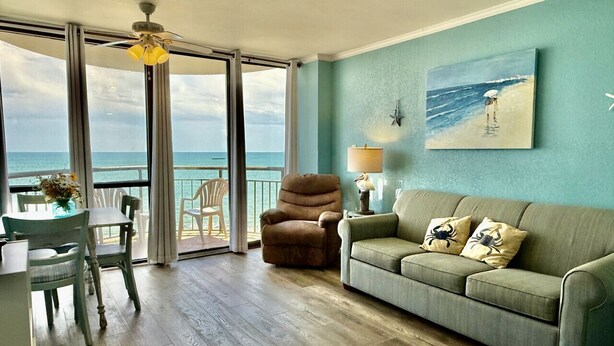Ein Wohnzimmer mit Meerblick, eine Couch, ein Sessel und ein Esstisch.