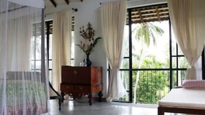 Quarto com cama, cómoda de madeira e uma janela grande com cortinas.