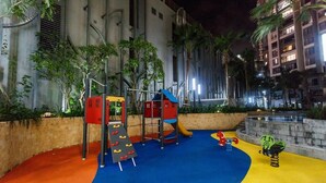 Un patio de recreo al aire libre con estructuras para escalar, toboganes y una zona de juegos con suelo acolchado.