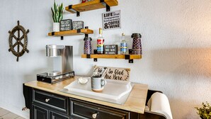 Eine Küche mit Holzböden, auf denen verschiedene Gegenstände stehen, eine Kaffeemaschine und ein Schild mit der Aufschrift 'Das Leben findet zwischen Kaffee und Wein statt'.