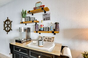 A kitchen with wooden shelves holding various items like a coffee machine, jars, and a sign that says "Life happens between coffee & wine."