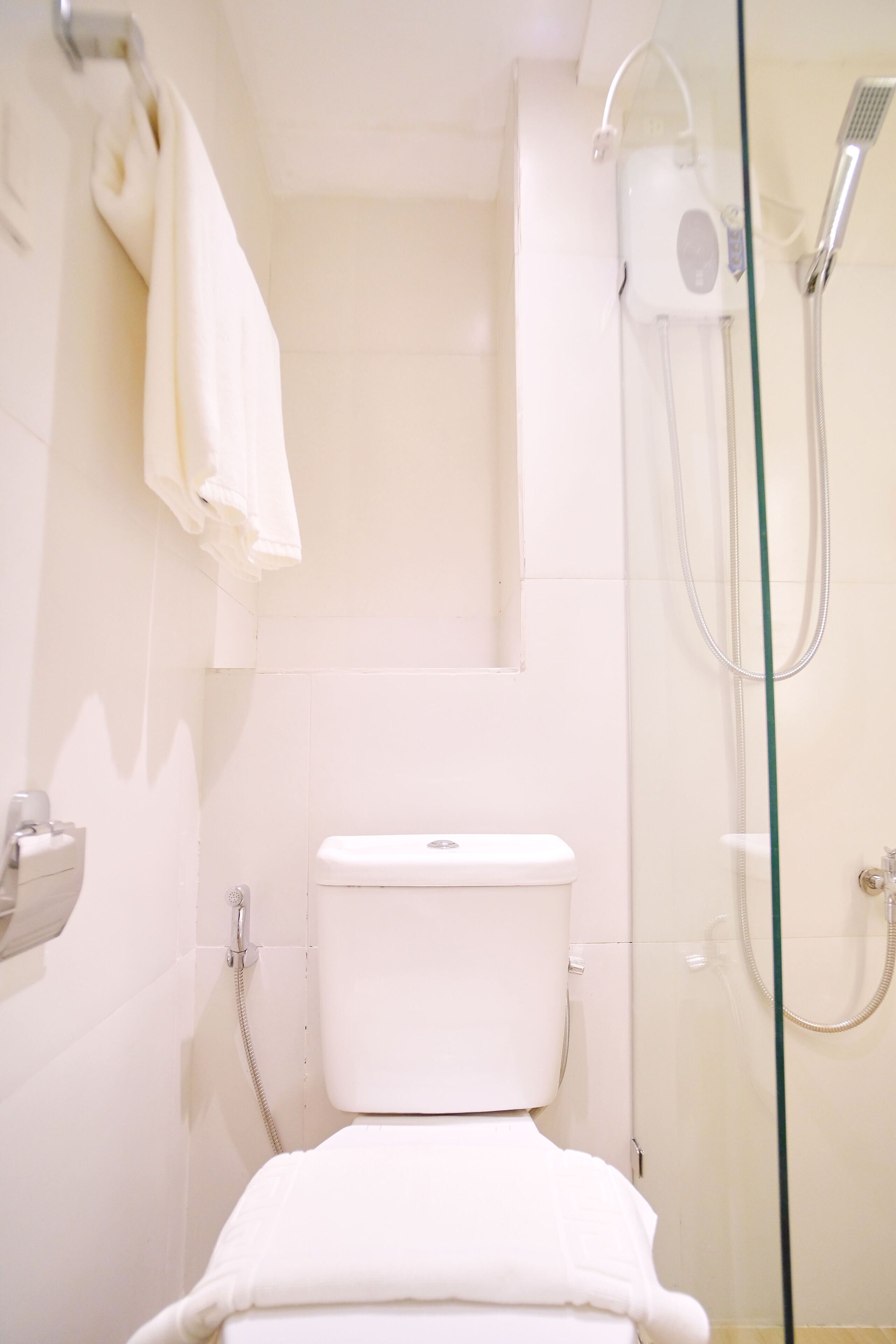 Un baño con inodoro, cabina de ducha de vidrio y toalla colgada en la pared.