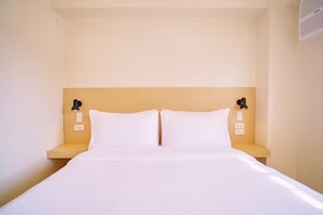 A hotel room with a single bed, two bedside tables, and wall-mounted reading lights.