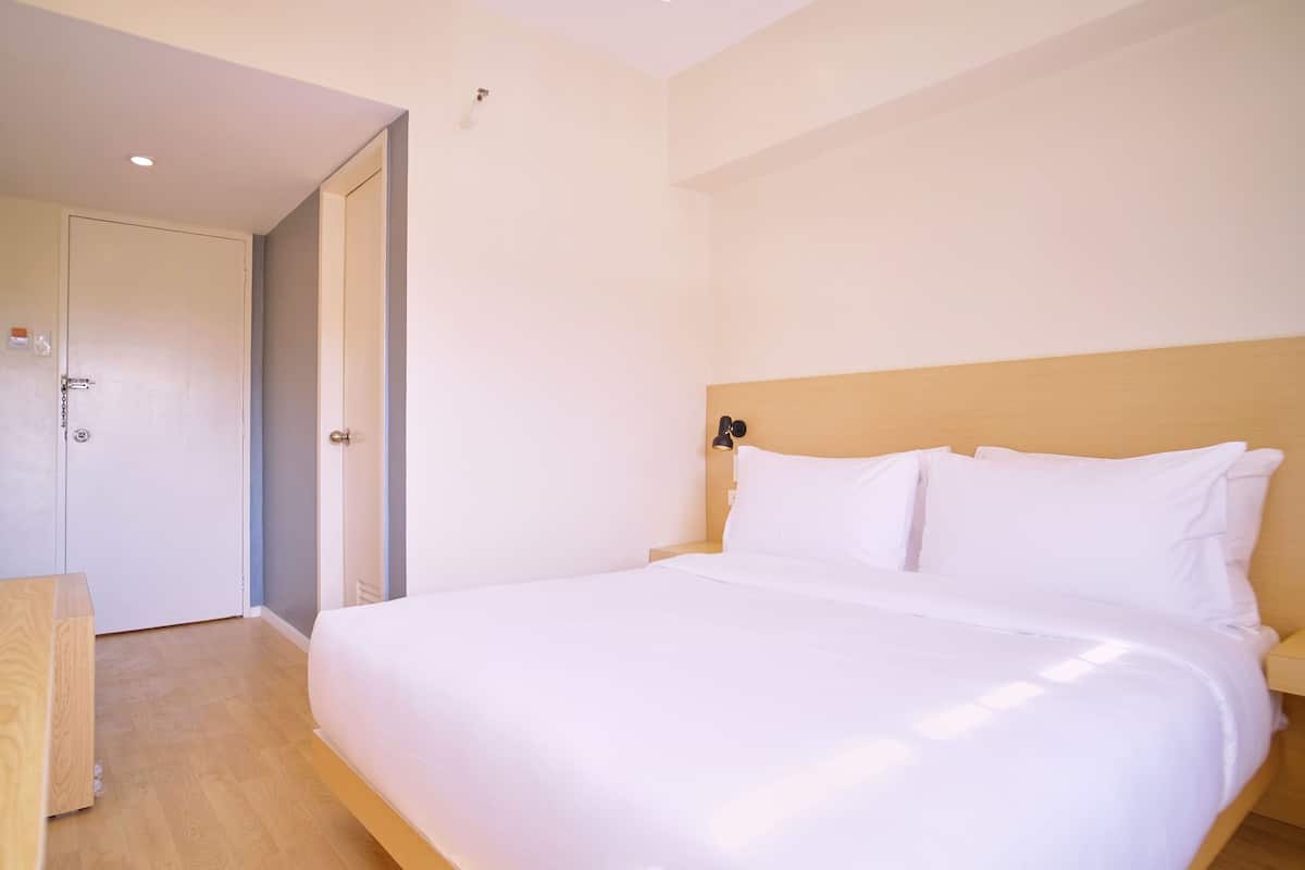 A hotel room with a large bed, a wooden headboard, and a door leading to another room.