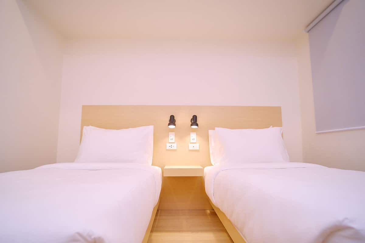 A twin room with two beds, a wooden headboard, bedside lamps, and a small shelf.