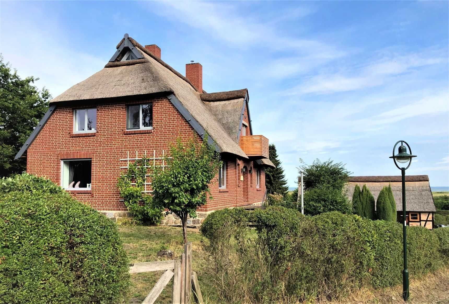 Ein Backsteinhaus mit Strohdach, einer Holztreppe und einem kleinen Garten.