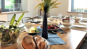 Una mesa de comedor con un jarrón de flores, un tazón de ensalada y un plato de pan.