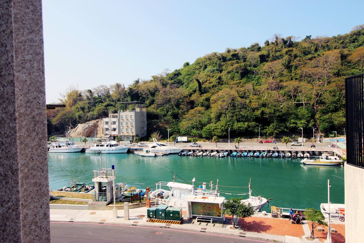 Uma marina com barcos atracados, uma torre de controle e uma encosta arborizada.