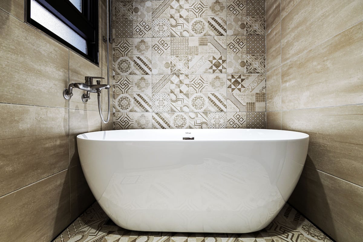 Uma casa de banho moderna com uma banheira independente, azulejos estampados e uma janela sobre a banheira.