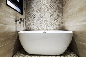 A modern bathroom with a freestanding bathtub, patterned tiles, and a window above the tub. - Hama Star (Kaohsiung)