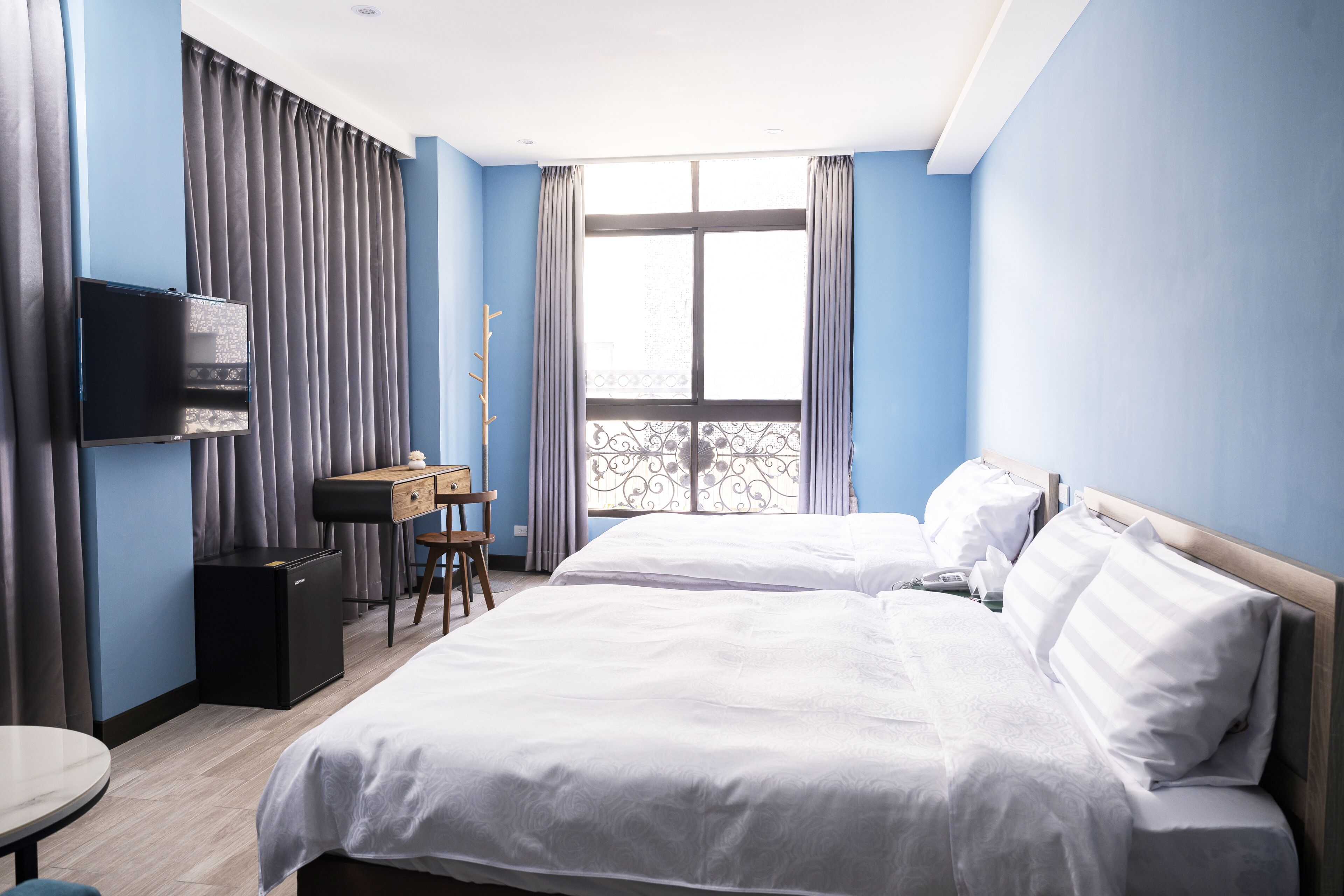 A hotel room with two beds, a desk, a TV, and a window with curtains.
