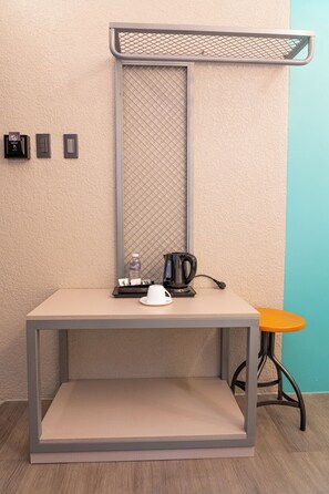 A small, modern kitchenette with a coffee maker, a kettle, and a water bottle on a table.