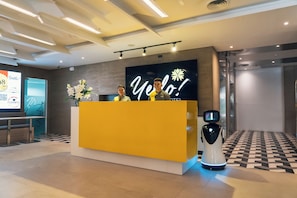 Ein Empfangsschalter mit einem digitalen Bildschirm, der eine Willkommensbotschaft, einen Roboter und eine Check-in-Theke zeigt.