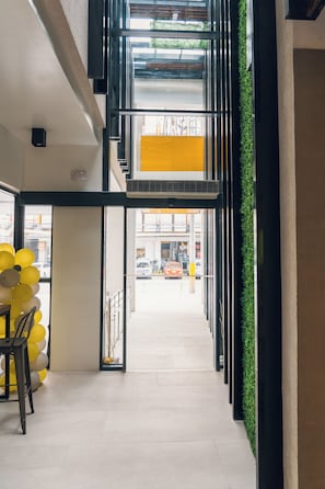 A modern interior with a staircase leading to a lower level, a yellow wall, and a view of the street outside. - Yello! Hotel (Cebu City)
