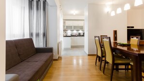 A modern living room with a sofa, a dining table with chairs, and a kitchen in the background. - Good Sleep Family (Kraków)