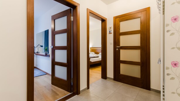 A hallway with wooden doors leading to a bedroom with a bed and a bathroom visible in the background. - Good Sleep Family (Kraków)