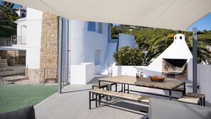 An outdoor patio with a wooden table and benches, a stone wall, and a white building with a chimney. - Sara 10 p.- modern, family friendly, private pool and tennis court! (Benissa)