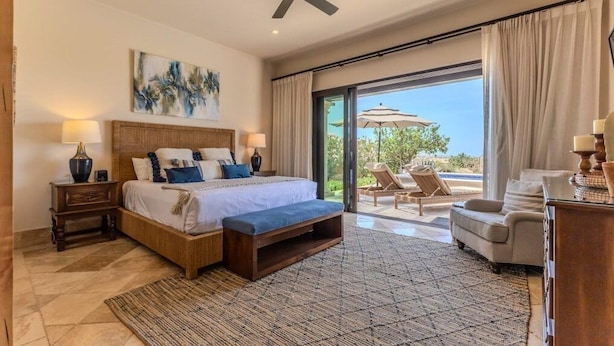 A spacious bedroom with a large bed, a ceiling fan, and a view of the outdoors through a sliding glass door.