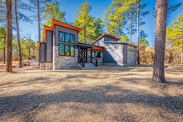 A modern two-story house with a stone facade and large windows, surrounded by tall trees.