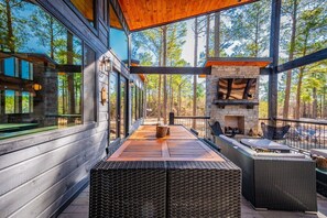 A modern outdoor patio with a stone fireplace, wicker furniture, and a view of the forest.