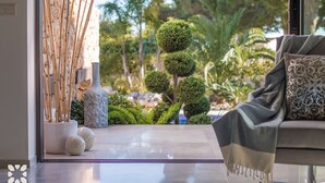 Een modern interieur met een glazen deur naar een tuin, met een bank, decoratieve vazen en een bonsaitje.