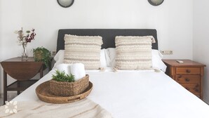 Een net opgemaakt bed met twee kussens, een nachtkastje met een vaas en een plant, en een nachtkastje met een telefoon en een lade.