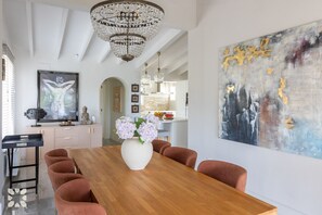 Un coin repas avec une table en bois, des chaises, un vase de fleurs, un lustre et des œuvres d’art accrochées aux murs.