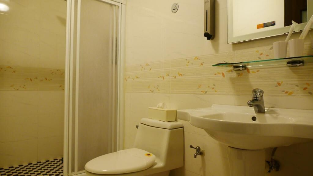 A bathroom with a toilet, sink, and glass shelf above the sink.