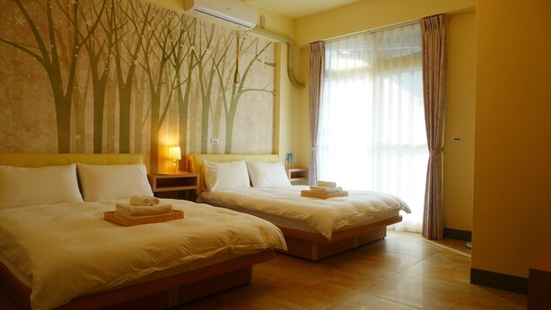 A hotel room with two beds, a large window with curtains, a wall with a tree mural, and a bedside table with a lamp. - Finest Hour Guesthouse (Chishang)