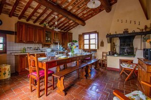 A rustic kitchen with wooden cabinets, a large dining table, and a fireplace.