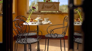 Un patio con sedie e tavoli in metallo, un piccolo tavolo con pasticcini e una tazza, e vista su un edificio con una scultura.