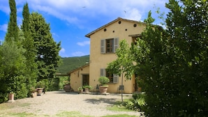 Un edificio a due piani con un cortile in ghiaia, piante in vaso e vista sul verde circostante.