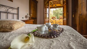 Un letto rifatto con cura, un cuscino decorativo, un vassoio con tazzine e teiera, e un fiore bianco sul coprimaterasso.