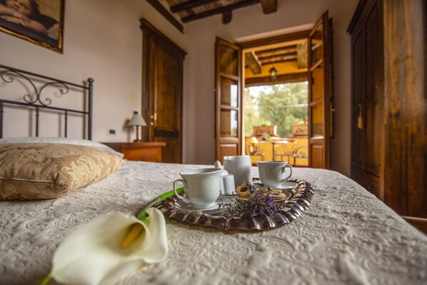 A neatly made bed with a decorative pillow, a tray with teacups and a teapot, and a white flower on the bedspread.