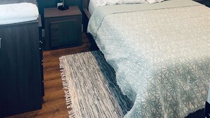 Un dormitorio con cama, mesitas de noche, lámpara y un cuadro en la pared.